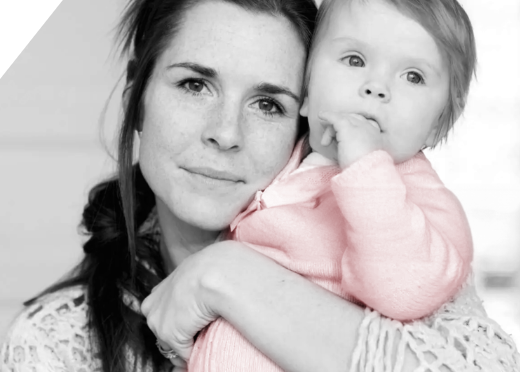 A black and white photo of a woman holding an infant who is wearing a pink onesie.