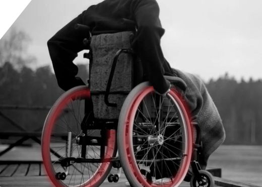 A black and white photo of a person in a wheelchair with red wheels.