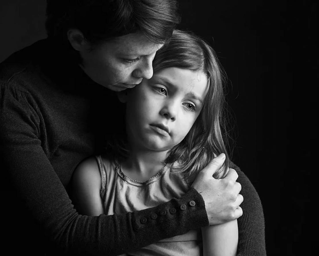A black and white photo of an adult woman hugging a young girl.
