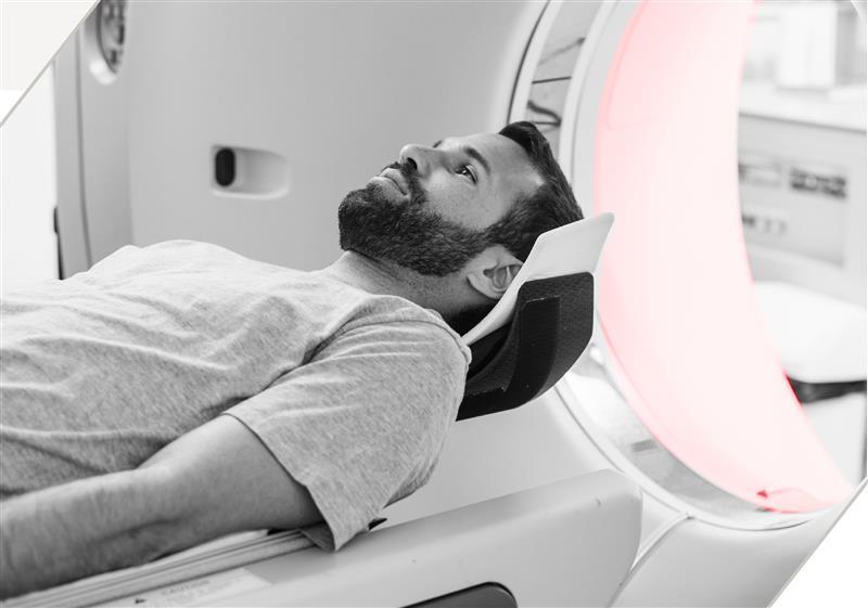 A bearded man lies on his back about to enter an MRI machine.