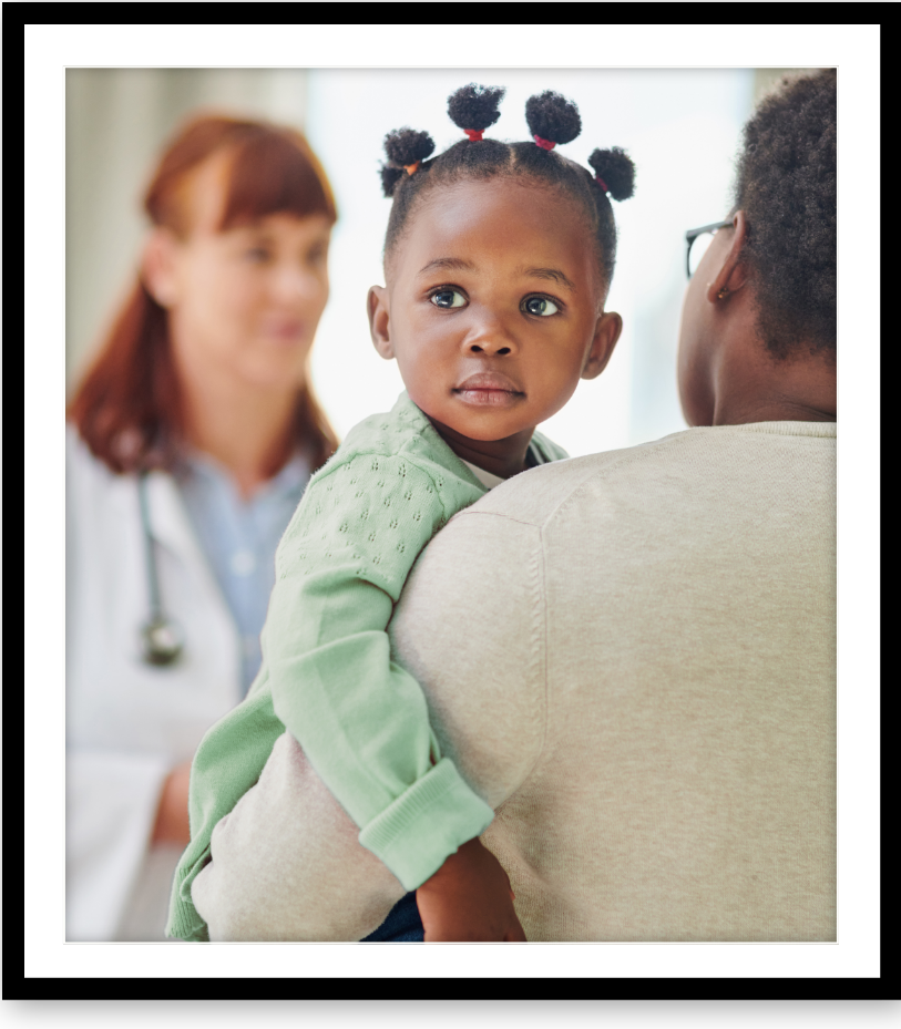 A young girl being held by a man, with a healthcare provider in the background.